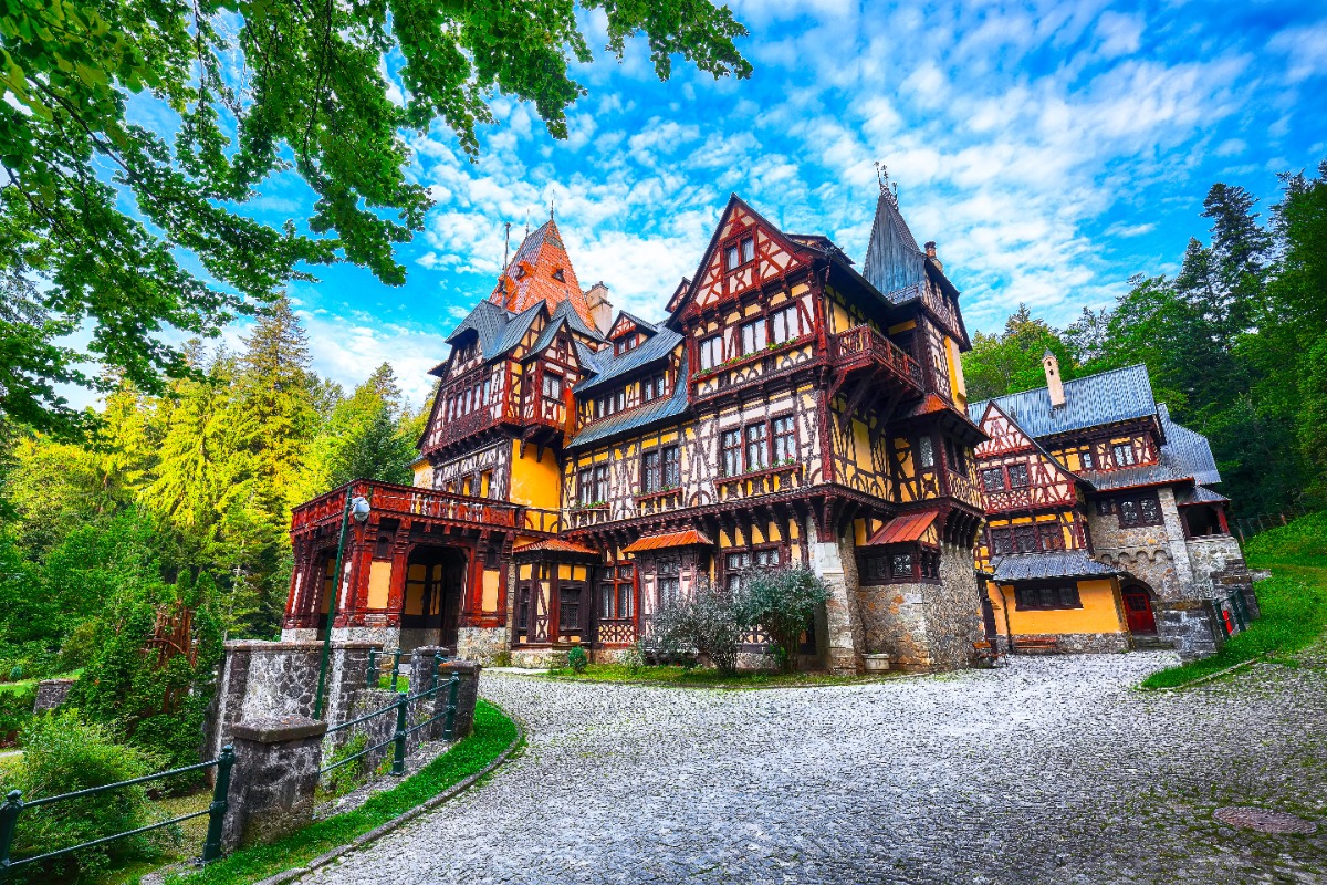 Colorful half-timbered castle in the forests of Transylvania, Romania, surrounded by lush green trees under a bright blue sky — a perfect setting for a luxury haunted getaway curated by Fort Collins travel advisor Amore Travel Designs