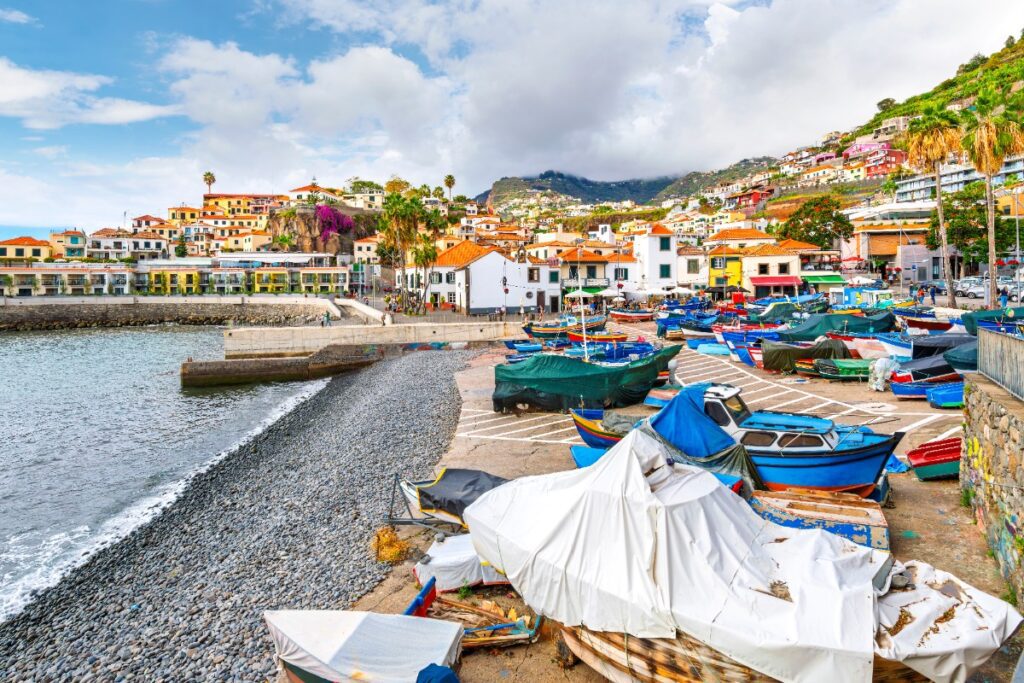 A colorful fishing harbor in Madeira, Portugal, with terracotta-roofed village houses climbing the lush volcanic hillside — a hidden Atlantic gem curated by Amore Travel Designs.