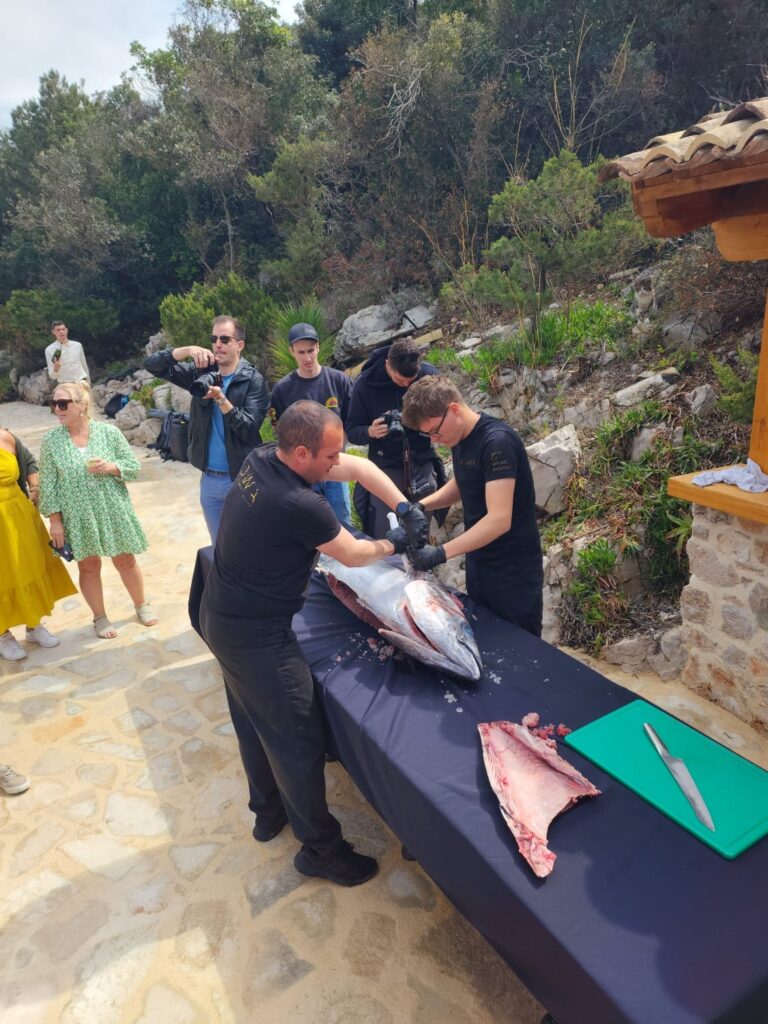 Tuna butchering demo outdoors; chefs at work, guests watching in a sunlit garden.
