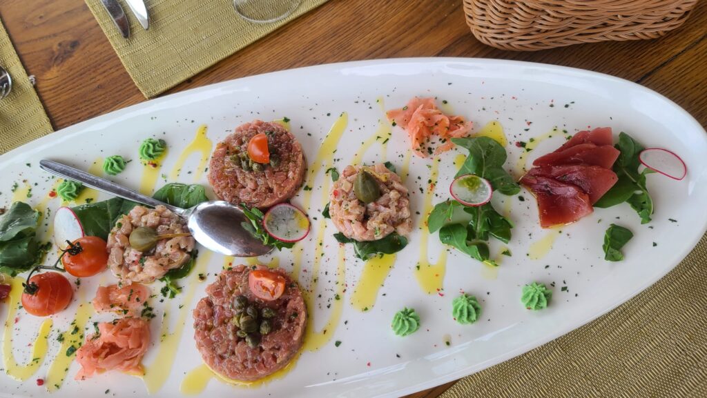 Fort Collins-based luxury travel advisor’s dining scene: raw fish tartare platter on a wooden table, greens, and olive oil drizzle.