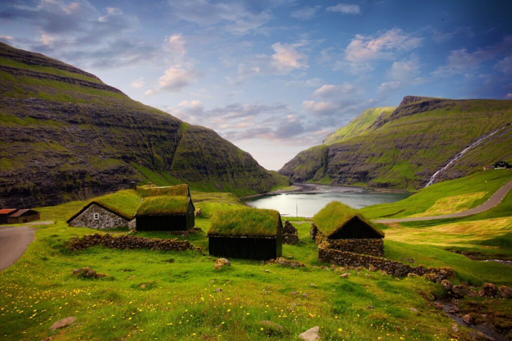 Traditional grass-roofed cottages nestled in a dramatic green valley in the Faroe Islands — one of Europe's most breathtaking hidden gem destinations, featured by Amore Travel Designs.