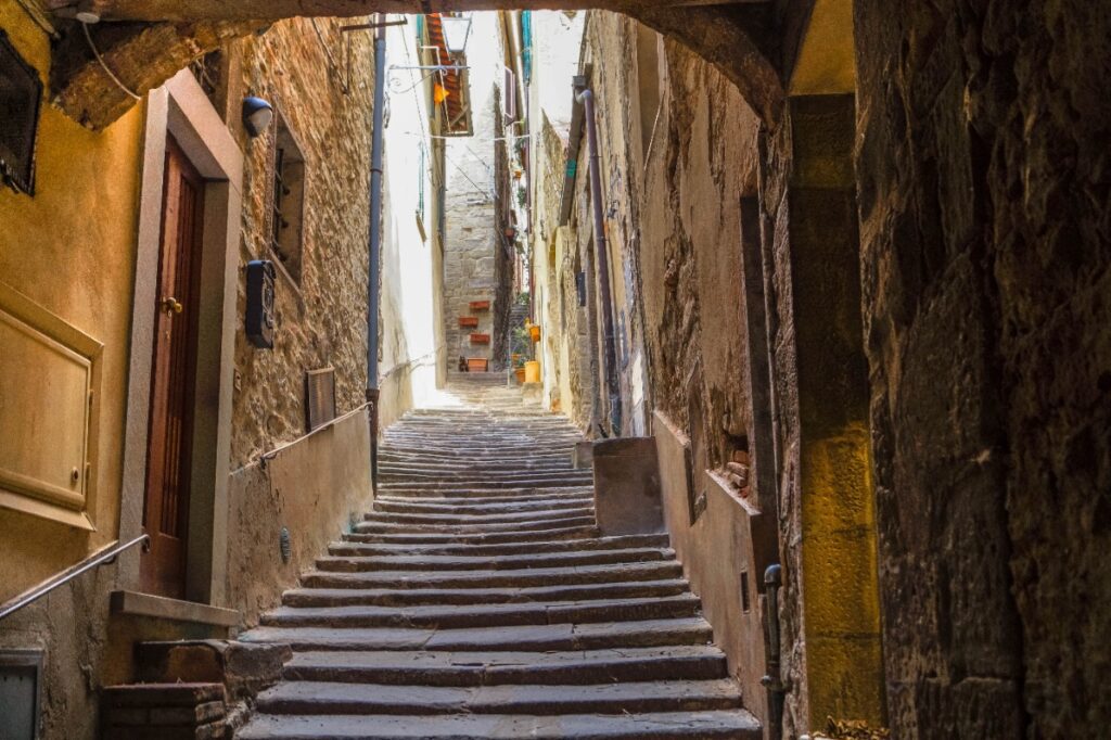 A sunlit alley in Cortona, Tuscany — the kind of street you wander down and suddenly understand why Diane Lane never went home